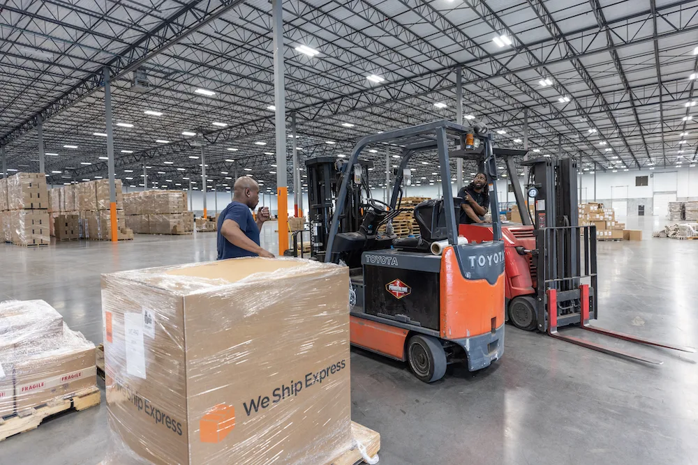 Fork lift operators talking to each other while preparing to pick up a pallet in a warehouse