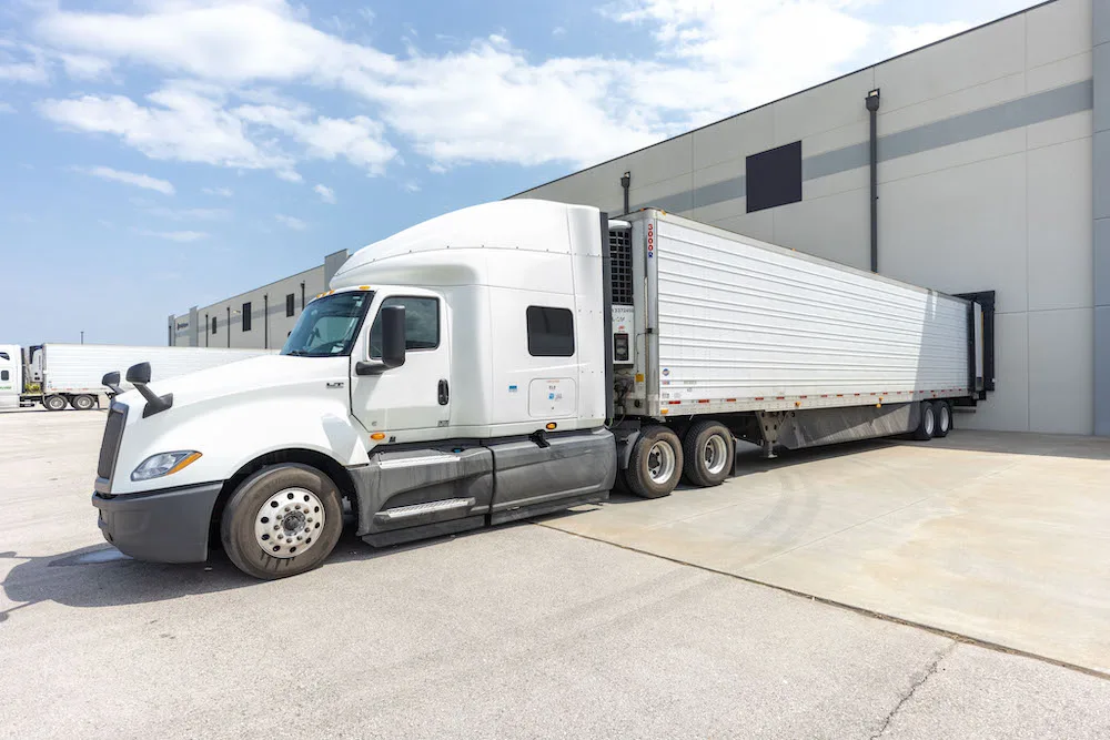 A white temperature-controlled line haul semi truck parked in a loading dock