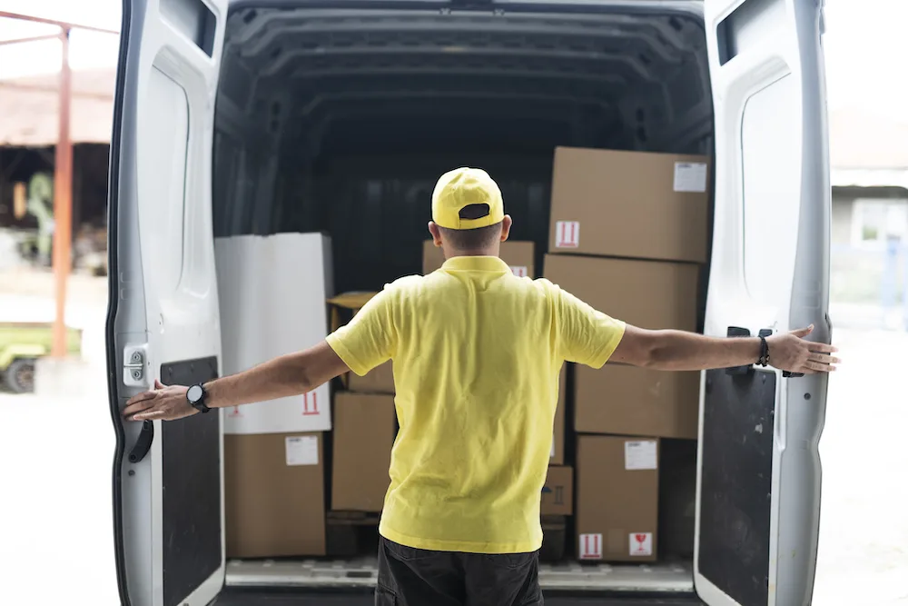 A delivery man opening the back of a delivery van filled with boxes.