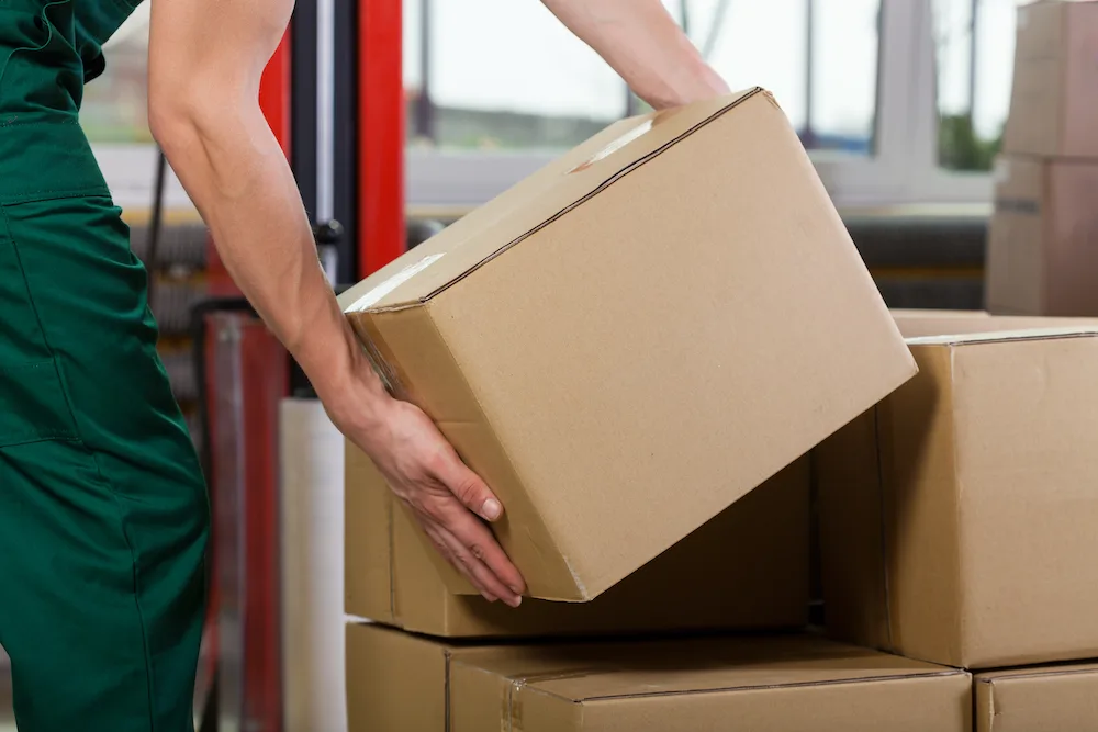 Hands of warehouse worker lifting box